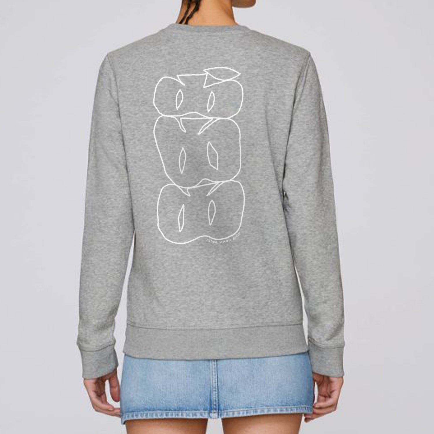 Photo of a model wearing a heather grey sweater. The print on the sweater is a white line art drawing of 3 cut apples on top of each other forming a stack.