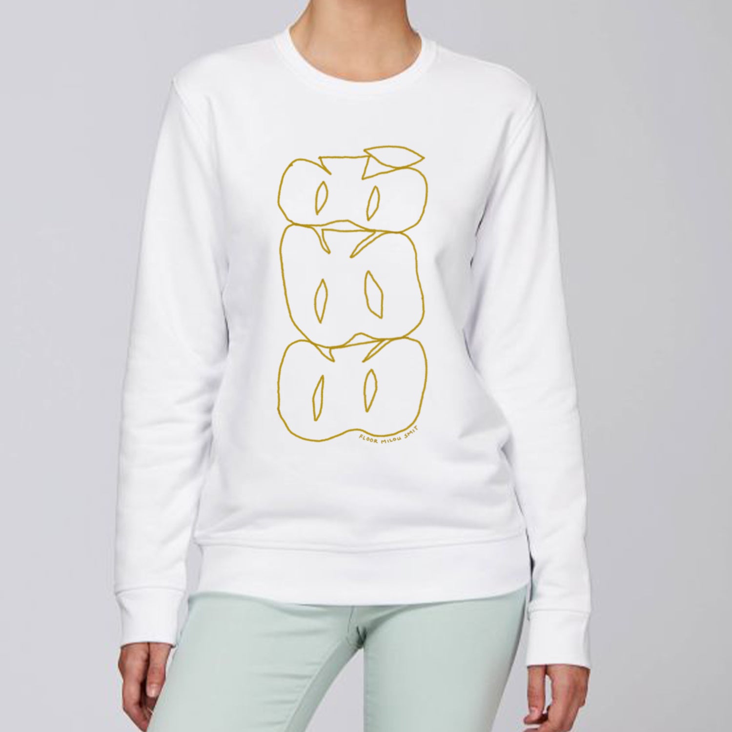 Photo of a model wearing a white sweater. The print on the sweater is a brown line art drawing of 3 cut apples on top of each other forming a stack.